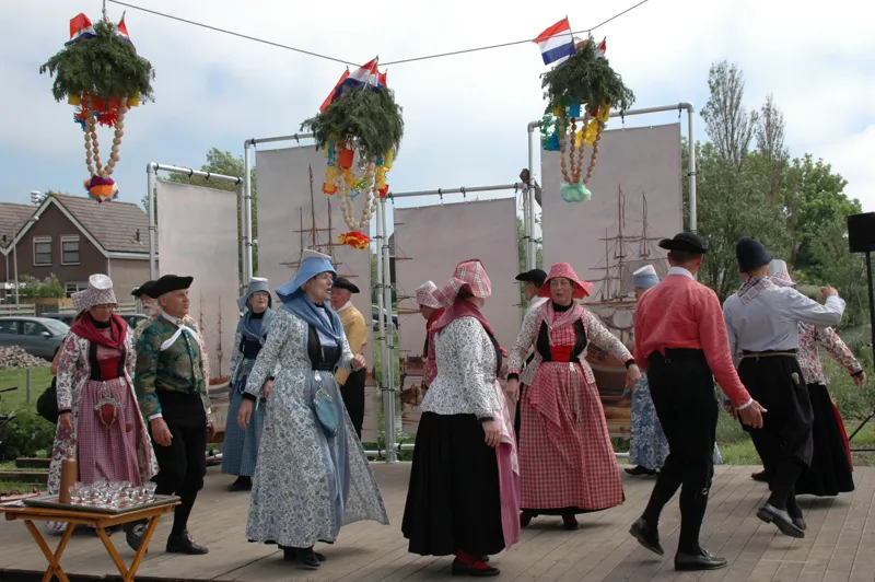 Dansers in Hindelooper klederdracht op een plein met bloemenkransen