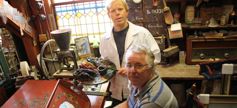 Twee schilders in een atelier vol beschilderd meubilair en gereedschap